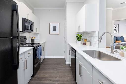A black refrigerator is in a white kitchen with a sink and a plant.