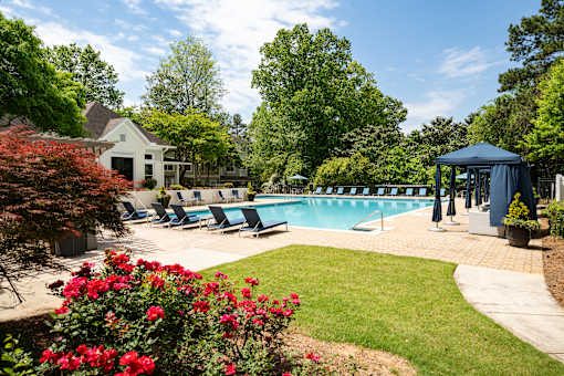 A pool surrounded by a lawn and trees with a house in the background.