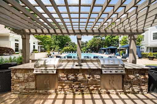 A grill is built into a stone wall under a wooden pergola.