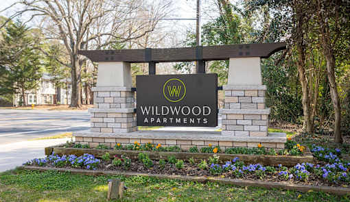 A sign for Wildwood Apartments is surrounded by flowers and greenery.