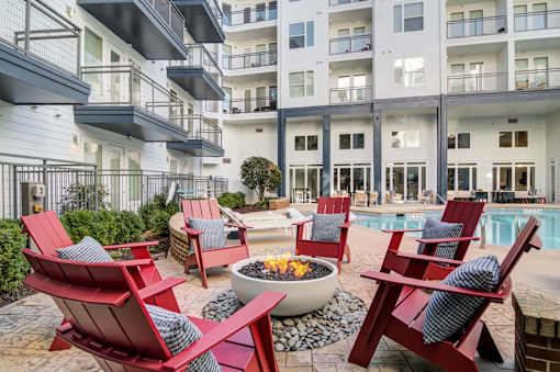A poolside area with red chairs and a fire pit.