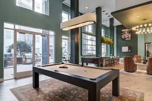 A pool table is in the middle of a room with a green wall and a large window.