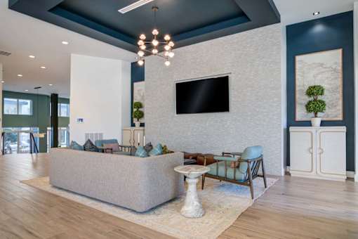 A modern living room with a grey sofa, a white coffee table, and a large flat-screen TV mounted on the wall.
