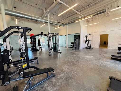 A gym with a variety of equipment including a weight bench, a leg press machine, and a squat rack.
