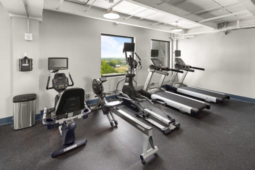 a room filled with cardio equipment and a window with a view of a city
