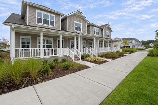 A row of houses with white railings and a sidewalk in front.