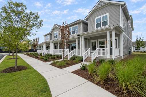 A grey house with a white porch and a tree in front.