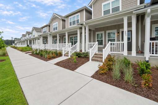 A row of houses with white railings and steps leading to the front door.