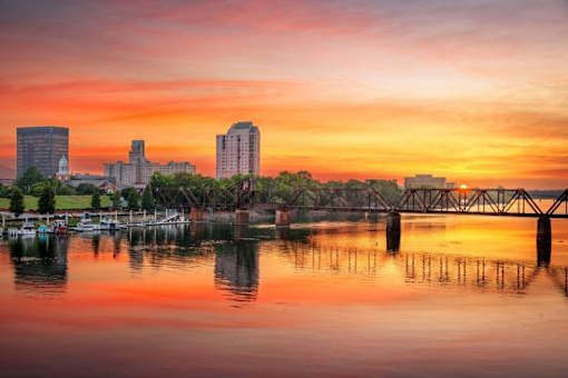 A city skyline is reflected in the water at sunset.