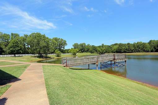A wooden bridge over a body of water with a grassy area on the left.