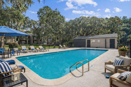 A pool surrounded by chairs and umbrellas with a building in the background.