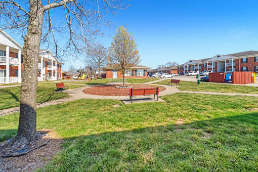 A park with a bench and a tree in the foreground and apartment buildings in the background.