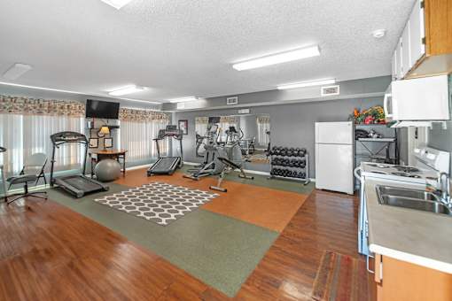 A spacious room with a variety of exercise equipment and a kitchen area.