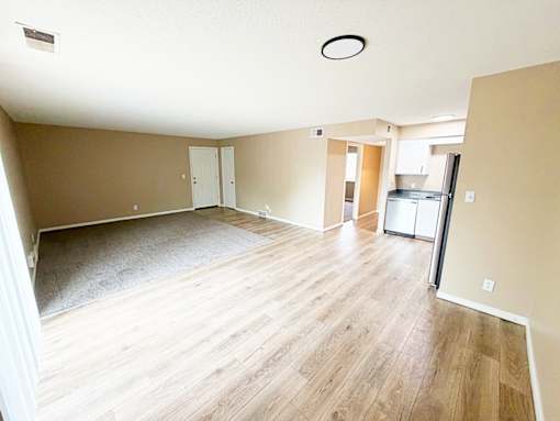 A spacious room with wooden flooring and a refrigerator in the corner.