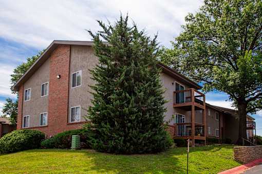 A large tree in front of a two-story apartment building.