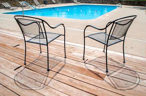 Two black chairs are on a wooden deck by a pool.