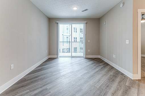A spacious room with light wood flooring and a view of a balcony through a glass door.at Tiffany Flats, Ohio, 43231