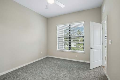 A room with a carpeted floor, a ceiling fan, and a window with blinds.