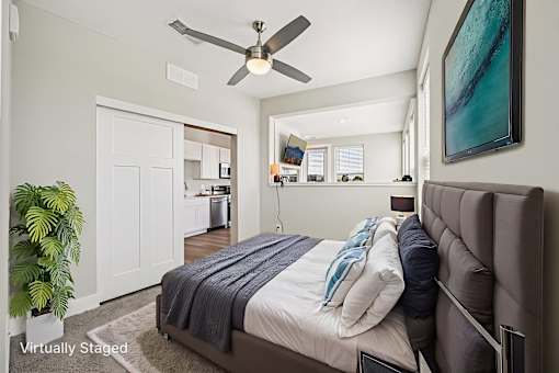 A bedroom with a bed, a ceiling fan, and a plant.