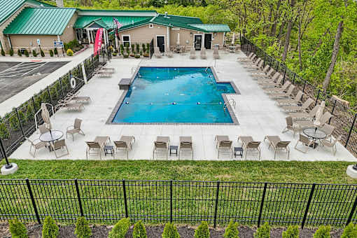 A large outdoor swimming pool surrounded by lounge chairs and a fence.