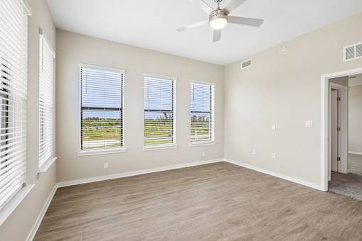 A room with a ceiling fan and three windows.