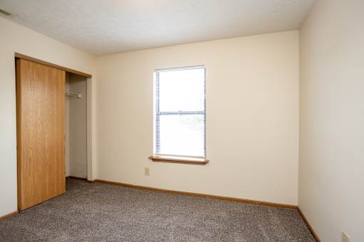 A room with a carpeted floor, a door, and a window with blinds.