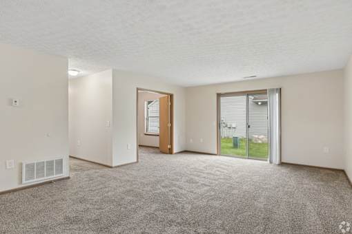 A spacious living room with a carpeted floor and a sliding glass door leading to a patio.