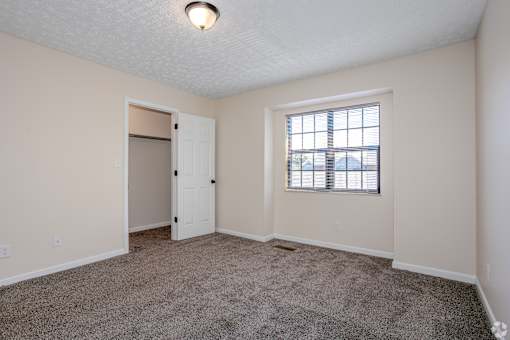 A room with a carpeted floor, a window with blinds, and a door.