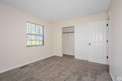 A room with a carpeted floor, a window with blinds, and a white door.