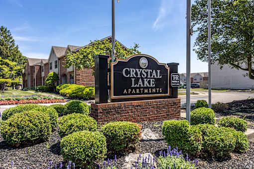 A sign for Crystal Lake Apartments is surrounded by bushes and flowers.
