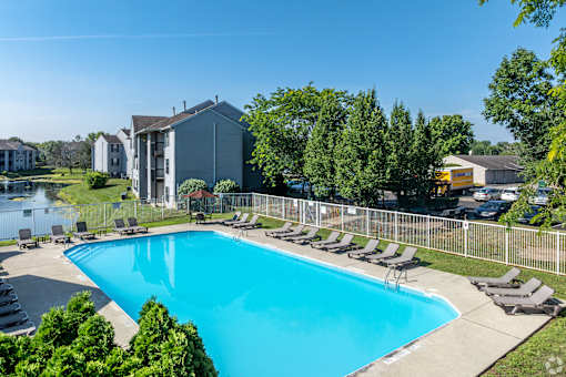 A swimming pool surrounded by lawn chairs and trees.