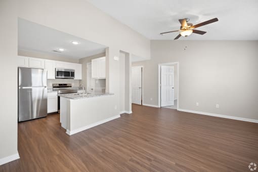 an empty living room with a kitchen and a ceiling fan