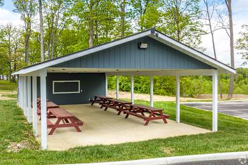 A pavilion with picnic tables is surrounded by trees.