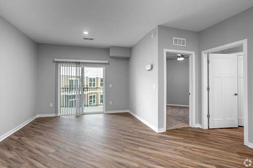 A room with a sliding glass door leading to a balcony, hardwood floors, and white walls.