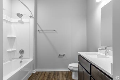 A white bathroom with a wooden floor and a white tub.