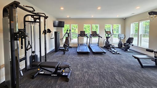 A spacious gym with a variety of equipment including treadmills, stationary bike, weights, and benches, located at the clubhouse at Greenwood Commons Apartments in Delaware, OH.