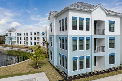 A modern two-story building with blue and white exterior and a black fence surrounding a grassy area.at Imperial Crossing Luxury Apartment Homes, Bonita Springs, FL