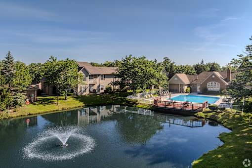 A fountain in the middle of a pond in front of a house.