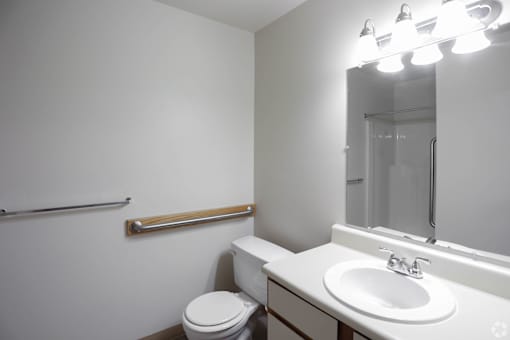 A white bathroom with a toilet, sink, mirror, and lights.