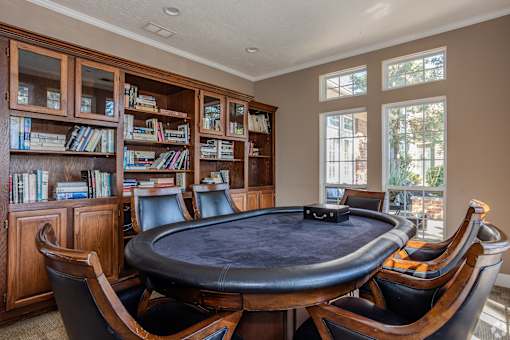 A poker table surrounded by leather chairs in a room with bookshelves.