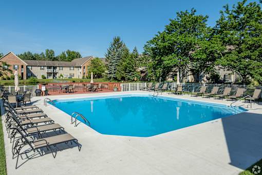 A large blue swimming pool surrounded by lounge chairs and trees.