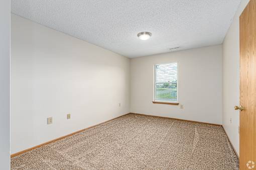 Carpeted bedroom and window with blinds of River Valley apartment home in Lancaster, OH.