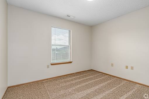 Carpeted bedroom and window with blinds of River Valley apartment home in Lancaster, OH.