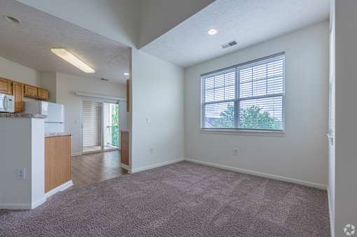 A spacious living room with a carpeted floor and a window with blinds.