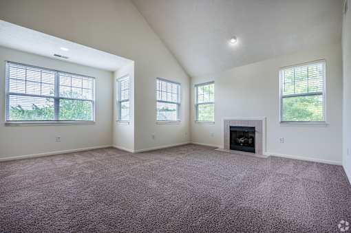 A large empty room with a fireplace and three windows.