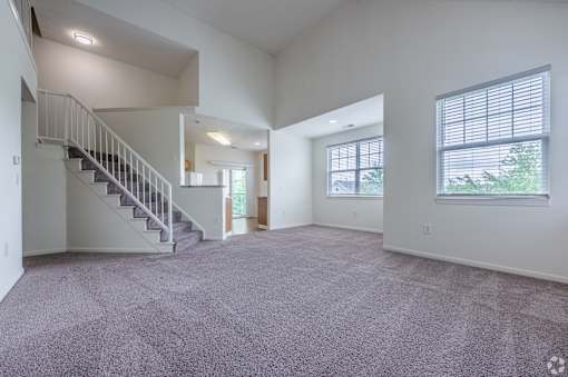 A spacious living room with a staircase and large windows.