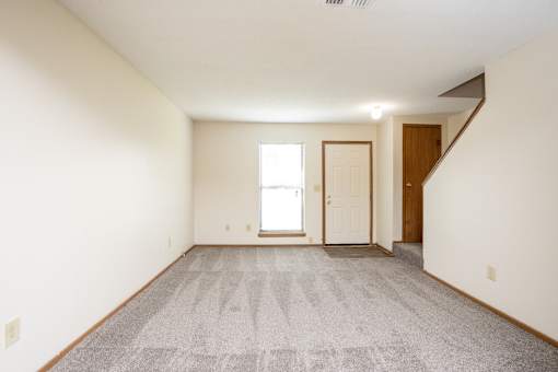 A room with a carpeted floor and a staircase on the right side.