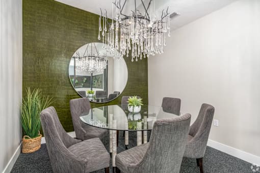 A dining room with a glass table and grey chairs.