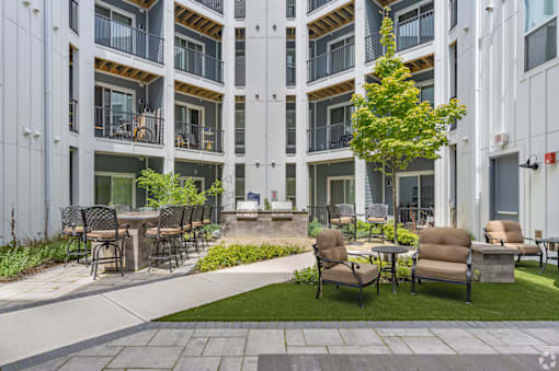 A patio area with chairs and tables is surrounded by apartment buildings.