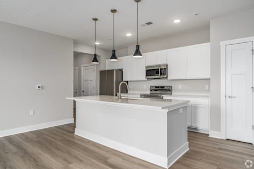 A modern kitchen with a white island and pendant lights.